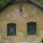 The exterior of an outdated home with peeling paint and dirty windows. The remaining paint is a dingy yellow color.
