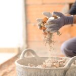 A close-up of a man with gloves dropping demolished stone and concrete into a large basket full of debris.