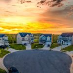 A cul-de-sac in a new construction neighborhood features eight two-story modern homes. The sun is setting behind them.