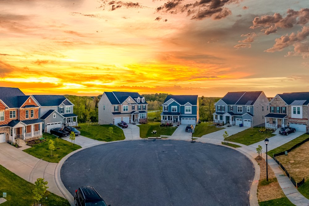 A cul-de-sac in a new construction neighborhood features eight two-story modern homes. The sun is setting behind them.