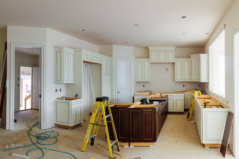 Kitchen undergoing a remodel with white cabinets, a brown kitchen island, a ladder, and green cables on the floor.