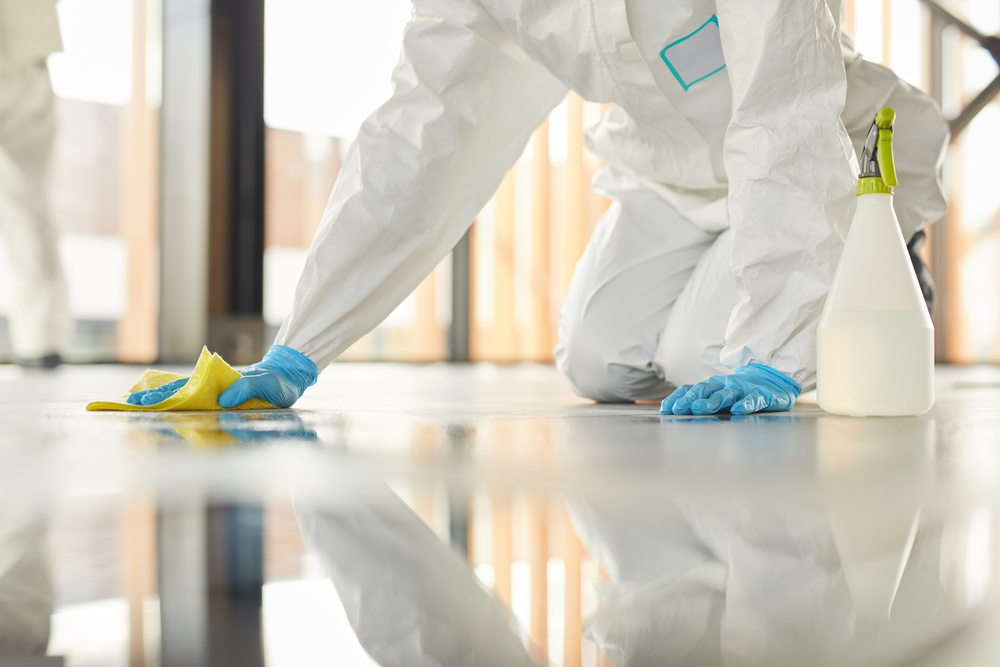 A person is kneeling on the ground and cleaning up a mess. They are wearing blue gloves and a white jumpsuit.