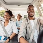 A happy family sitting in the car together. The parents are in the front seat with Dad behind the wheel.
