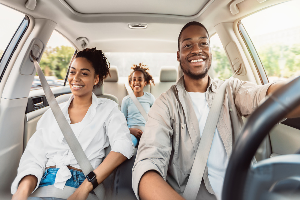 Home 8 A happy family sitting in the car together. The parents are in the front seat with Dad behind the wheel.