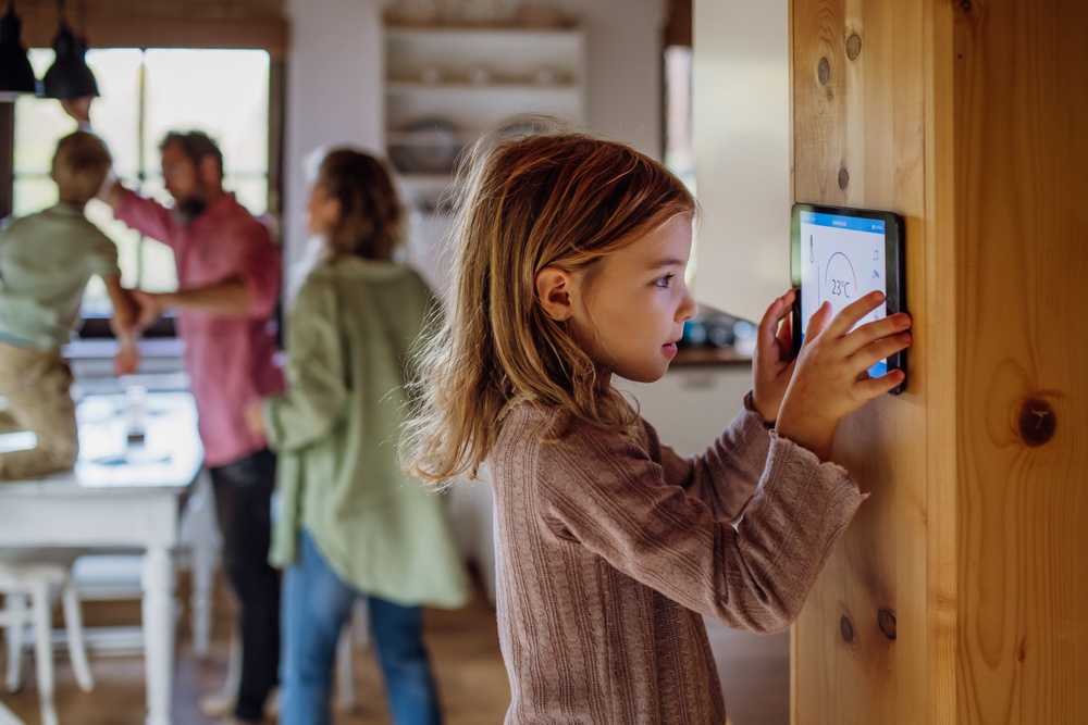 A little girl looking closely at a digital screen placed on the wall inside a kitchen with her family in the background.