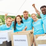Five people wearing blue volunteer shirts standing behind donation boxes, cheering enthusiastically.