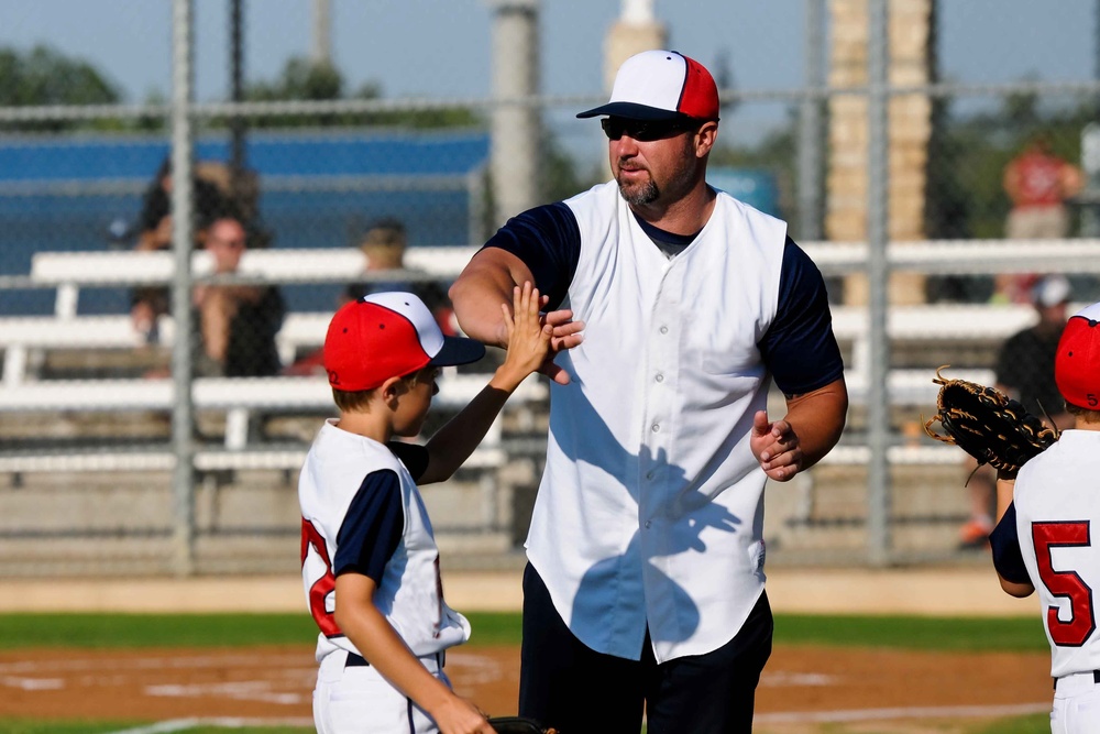 A little league baseball manager in a white vest jersey in a white hat high-fives a youth player in the same jersey.