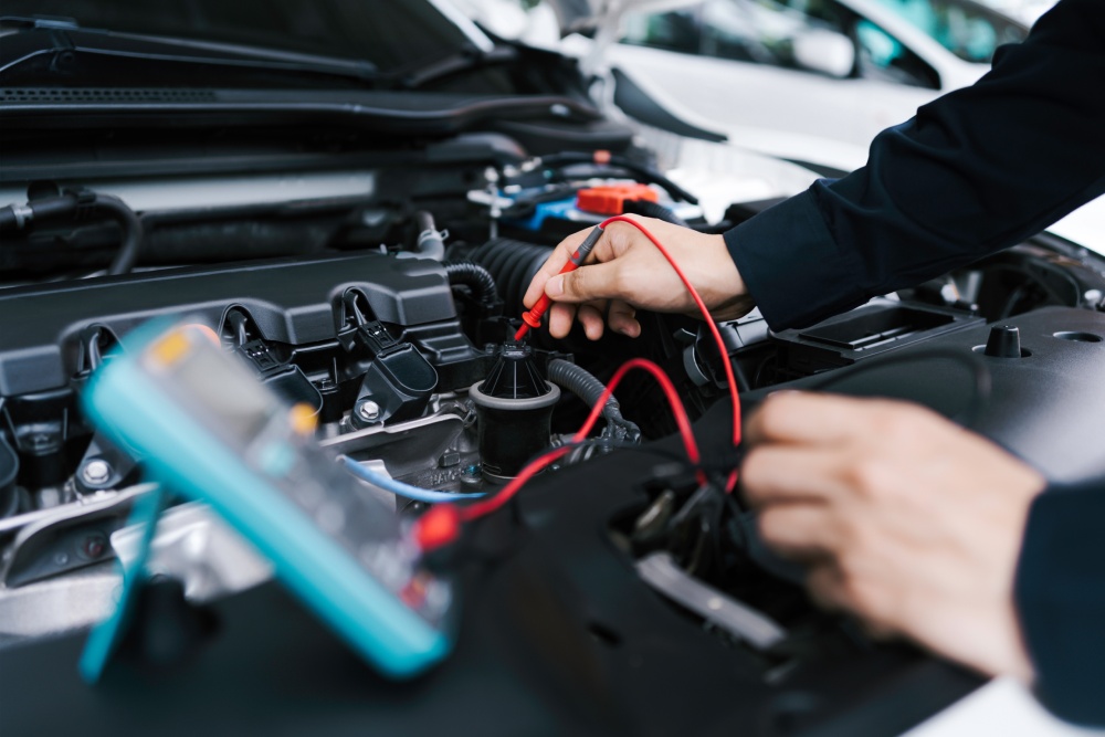 A technician using a small red tool connected to a blue device to repair a car battery in a brightly lit shop.