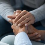 A close-up of the hands of two women, one older than the other, gently clasped to provide comfort.