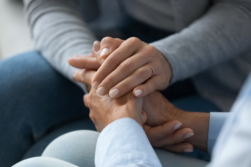 A close-up of the hands of two women, one older than the other, gently clasped to provide comfort.